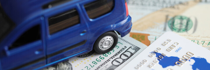 Blue toy car standing on dollar bills and plastic credit card closeup