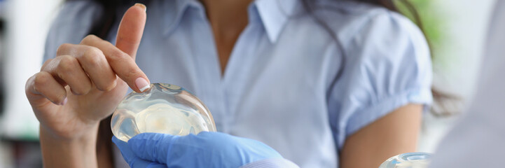 Female patient touching silicone implant on doctor hand with her finger closeup