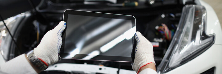 Master repairman holding digital tablet near open hood of car closeup