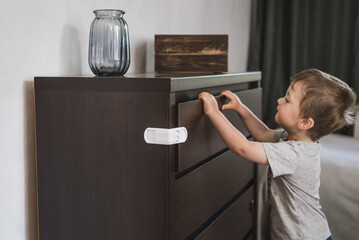 Child unsupervised plays with cabinets. Danger for the baby to pinch the hand of the cabinet door. Protect children from home furniture kids safety. Selected focus