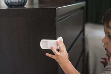 Child unsupervised plays with cabinets. Danger for the baby to pinch the hand of the cabinet door. Protect children from home furniture kids safety. Selected focus