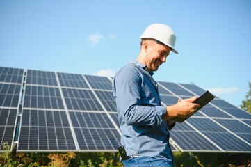 The portrait of a young engineer checks with tablet operation with sun, cleanliness on field of photovoltaic solar panels. Concept: renewable energy, technology, electricity, service, green power - obrazy, fototapety, plakaty