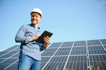 The portrait of a young engineer checks with tablet operation with sun, cleanliness on field of photovoltaic solar panels. Concept: renewable energy, technology, electricity, service, green power