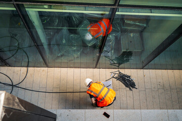 Top down view on a construction site worker in orange high visibility vest and white hard safety...