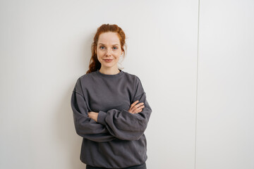 young redhead woman standing with crossed arms in front of white wall