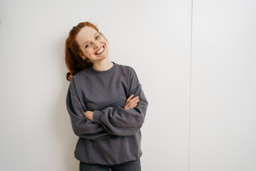young redhead woman stands laughing with folded arms in front of white wall