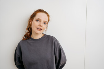 young redhead woman in front of a white wall and looks promptly into the camera