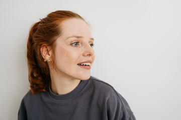 young redhead woman in front of white wall and looks to the side