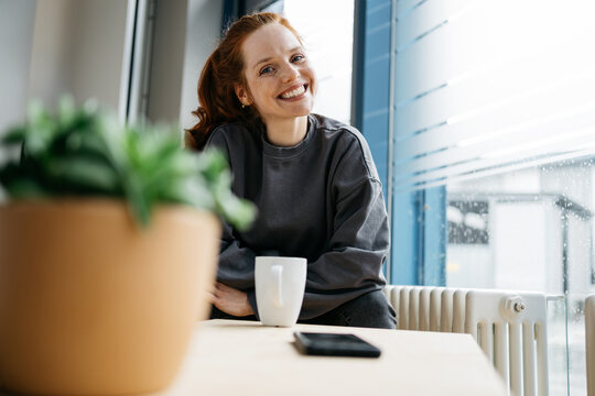 young redhead woman takes break in her office and looks at camera laughing