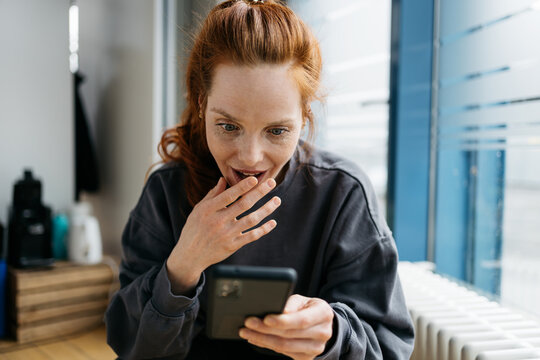 young redhead woman looks at her cell phone in amazement