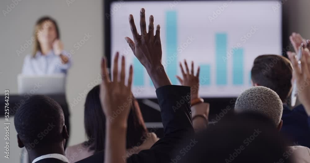 Poster audience of business people asking the speaker a question while lifting their hands during conferenc