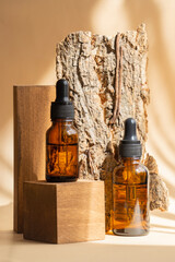 Two amber glass bottles with serum with dropper lids on wooden 3d podium against piece of tree...