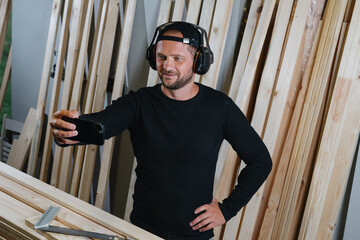 A carpenter takes a selfie on his phone in his workshop. Opening of a new workshop, a photo for memory