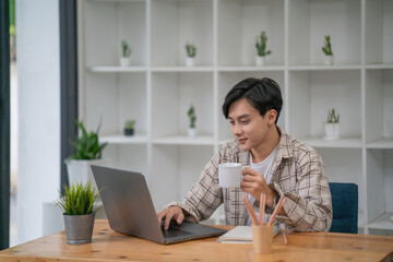 Asian businessman holding a coffee mug working on laptop at office.