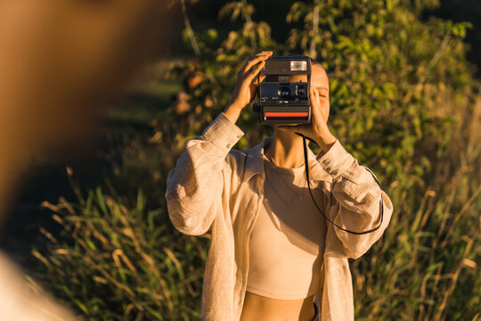 A young girl taking photos of her friend with an instant vintage camera. Weekend in nature at the summer sunset time . High quality photo