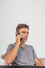 A young guy sits scared talking on the phone while sitting in a chair on a white background