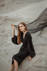 A beautiful girl in a black dress and a developing cloth on the background of the desert. A beautiful mysterious blue-eyed girl in a black dress on the background of the desert.