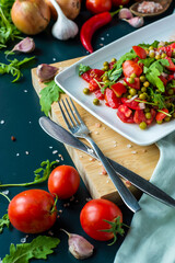 summer salad, tomatoes, green peas, arugula, onion, olive oil, garlic, hot pepper fork knife bamboo cutting board pastel green napkin  textile, salt Vegetarian vegan food,