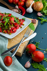 summer salad, tomatoes, green peas, arugula, onion, olive oil, garlic, hot pepper fork knife bamboo cutting board pastel green napkin  textile, salt Vegetarian vegan food,