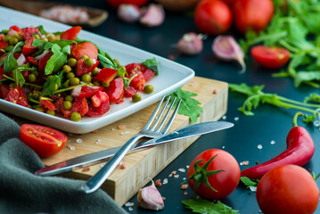 summer salad, tomatoes, green peas, arugula, onion, olive oil, garlic, hot pepper fork knife bamboo cutting board pastel green napkin  textile, salt Vegetarian vegan food,