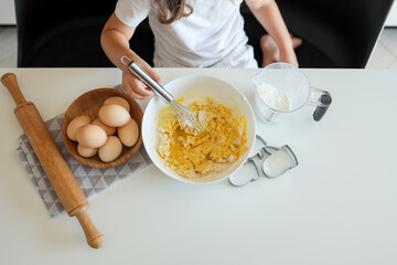 Child cook stirs dough for biscuits with a whisk