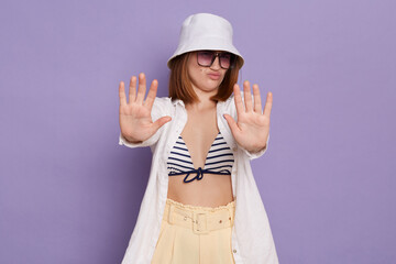 Portrait of serious strict woman wearing panama, white shirt and swimming suit, posing isolated...
