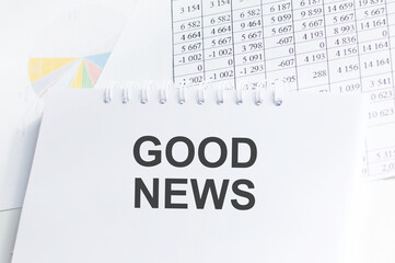GOOD NEWS inscription on a notebook on the background of reports and charts