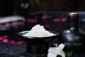 Bath salt in the bowl and bath foam in ceramic bottle on bathtub full of rose petals. Spa concept. Skin care treatment in spa salon. Wellness, healthy lifestyle, relaxation procedure. Selected focus.