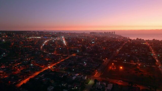 Aerial parallax of Concon neighborhood buildings illuminated at night near sea shore at colorful golden hour, Valparaiso, Chile
