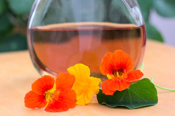 A composition presenting fresh nasturtium flowers with a bottle of filtered nasturtium tincture in a slightly orange color. Shallow depth of field.