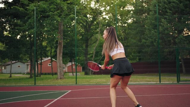 athletic lady in short black skirt is hitting tennis ball on court, sportive lifestyle and hobby