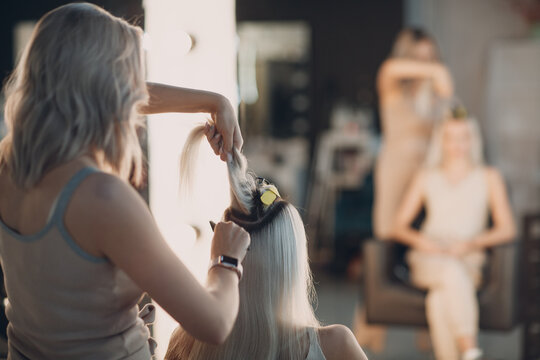 Hairdresser female making hair extensions to young woman with blonde hair in beauty salon. Professional hair extension