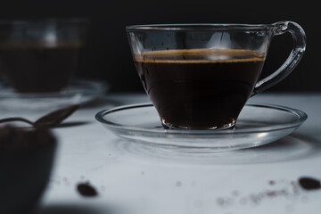 Contemporary style coffee food and drink photo. Set against a white background. Black coffee in glass cup and saucer.
