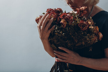Upset elderly woman hold withered dry old rose flowers bouquet. Old age Concept Symbol.