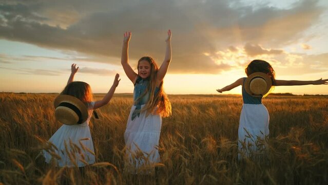 happy slavic children girls are whirling on golden rye field in sunset in farmland, little sisters
