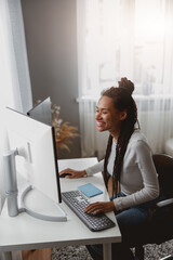 Smiling beautiful mixed-race female freelancer working on computer looking on screen at home