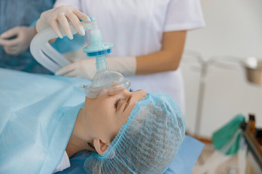Close up hands of doctor anesthesiologist holding breathing mask on patient face during operation