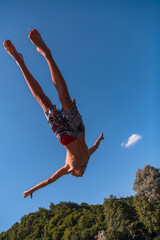 Young teen boy jumping flying and diving in the river. Clear blue sky and trees in distance as a...