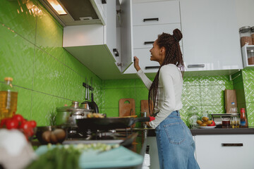 Side view of mixed-race beautiful woman opening kitchen cabinet, cooking concept