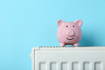 Piggy bank on heating radiator against light blue background, space for text