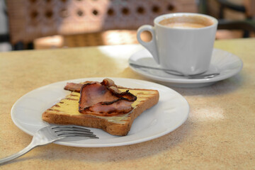 Cup of coffee and delicious sandwich with fried bacon on beige table