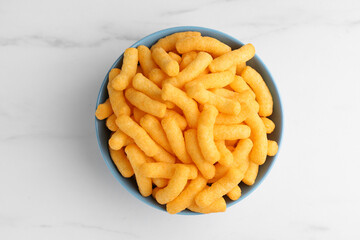 Bowl of tasty cheesy corn puffs on white marble table, top view