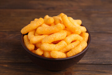 Bowl with crunchy cheesy corn snack on wooden table, closeup