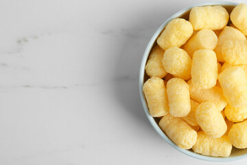 Bowl of delicious crispy corn sticks on white marble table, top view. Space for text