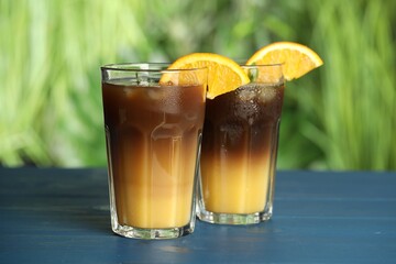 Tasty refreshing drink with coffee and orange juice on blue wooden table against blurred background