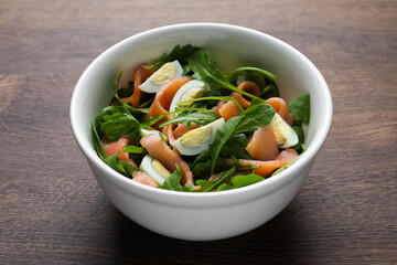 Delicious salad with boiled eggs, salmon and arugula on wooden table, closeup