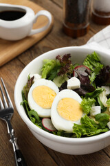 Delicious salad with boiled egg, feta cheese and vegetables on wooden table, closeup