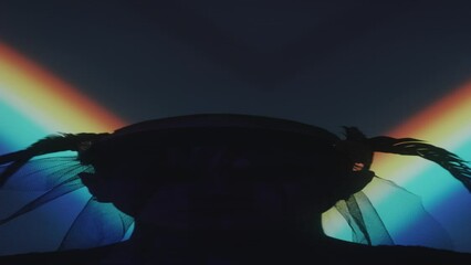 Vertical portrait of tattooed man with candle lit wreath on his head and painted nails holding palms together and posing for camera in dark studio with rainbow light projection - Powered by Adobe