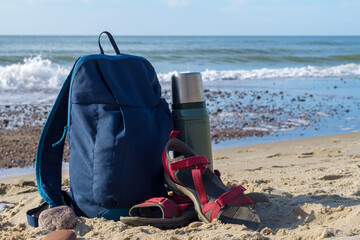 A thermos of tea and a backpack against the backdrop of nature. Walking along the seashore.