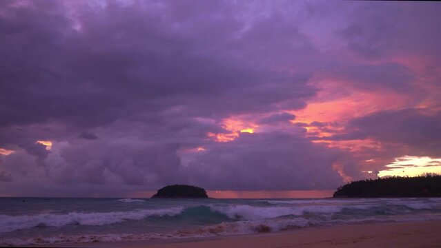 smooth waves hit on the beach at puple sunset..purple clouds cover the ocean during colorful cloud in sunset at Kata beach Phuket..video 4K. Scene of pink light in the sky background..